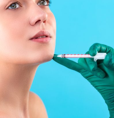 Beautiful woman face and beautician hands with syringe. Doctor makes cosmetic injection. Clean Beauty concept.